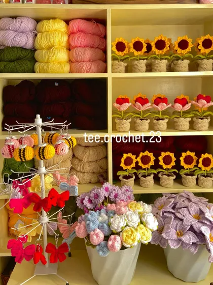 My workshop corner, showing yarn, amigurumi bees, and rows of potted sunflowers and heart flowers.