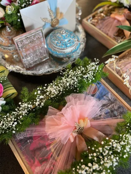 A close-up of the beautifully wrapped gift box, part of a Samdhi invitation. The box is adorned with a large pink tulle bow and surrounded by fresh baby's breath for a delicate finish.