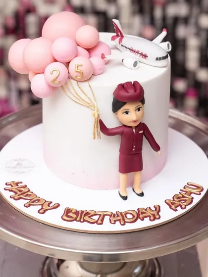 A chic and simple cake for a 25th birthday, themed around a flight attendant's career. The design features a figurine in uniform, an airplane, and pink balloons.