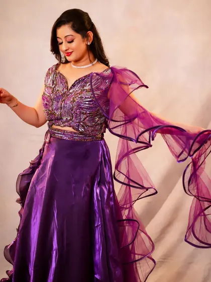 This studio shot focuses on movement and texture. The flowing ruffled sleeve of the purple lehenga creates a dynamic shape, and the detailed embroidery on the blouse is highlighted by the soft studio lighting.