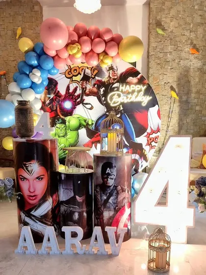 A DC and Marvel comics superhero theme for a 4th birthday. This indoor setup includes a dynamic backdrop with Hulk, Iron Man, and Captain America, plus a Wonder Woman prop.