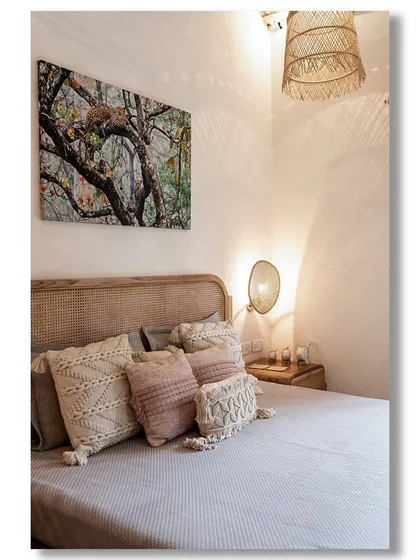 A serene bedroom in a Goan villa, with a rattan headboard, macrame cushions, and a woven lampshade that casts beautiful shadows. The space is a perfect example of relaxed, bohemian luxury.