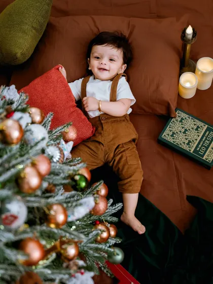 A cozy and classic Christmas portrait. This little one is captured in a warm, rustic setting with a beautifully decorated tree, soft candlelight, and vintage props, creating a timeless holiday memory.
