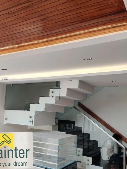 A modern staircase area with clean white walls, a polished wood ceiling, and glass railings. A perfect paint job is crucial in minimalist designs like this.
