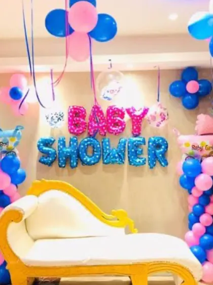 A baby shower decoration with a 'Baby Girl' and 'Baby Boy' theme. The setup includes balloon pillars and foil letters against the wall.