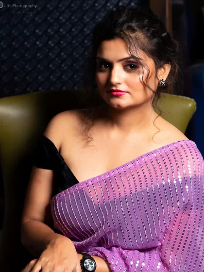An off-shoulder blouse paired with a sequined purple saree for a modern glamour look. The soft lighting and intimate pose create a sophisticated and alluring portrait.