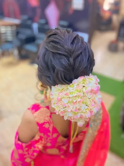 A braided updo finished with a large gajra of artificial flowers. This is a beautiful style for a traditional ceremony, combining a classic braid with a floral bun.