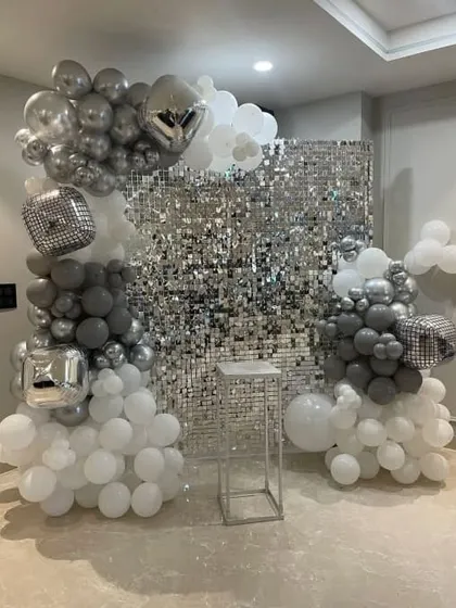 A silver sequin wall provides a fantastic backdrop for photos. Here, I've used an asymmetrical balloon garland in shades of grey, white, and silver, including disco ball foil balloons for extra sparkle.