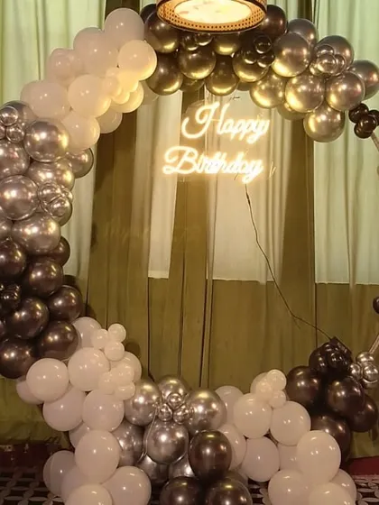 A sleek birthday balloon ring in a gradient of black, silver, and white, with a "Happy Birthday" neon sign.