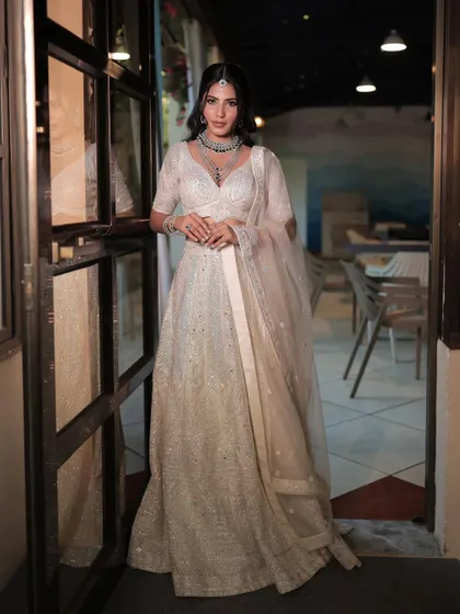 A full-length shot of an elegant white lehenga, perfect for a reception or engagement. The look is accessorized with a simple yet striking diamond necklace set.