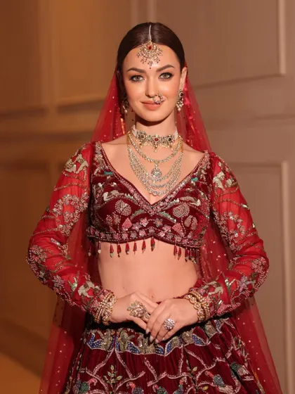A smiling bride, radiating joy in her traditional red velvet attire. The double dupatta draping adds to the grandeur.