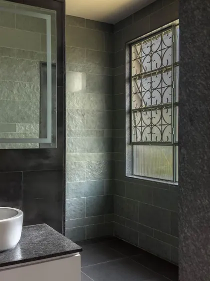 In this bathroom, we used dark, leather-finished Kota stone for the walls and countertop. A tall window with an ornamental grill provides privacy while allowing natural light to filter in.