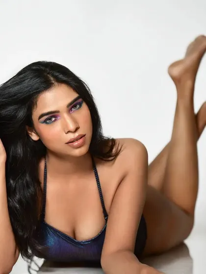 A playful pose from a bodysuit shoot, showcasing a creative and colorful eye look. The vibrant eyeshadow adds a pop of color that complements the iridescent fabric of the outfit.