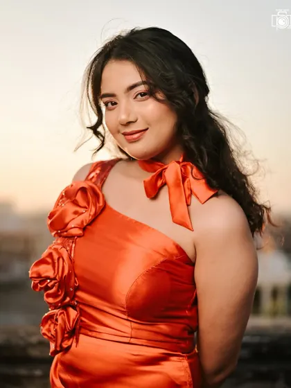 An outdoor shot taken during the golden hour, where the warm sunlight gives a soft glow to the model's skin. The vibrant red dress looks stunning against the evening sky.