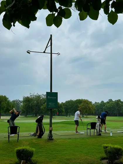 A view of the range through the leaves, showing golfers scattered across the practice area.