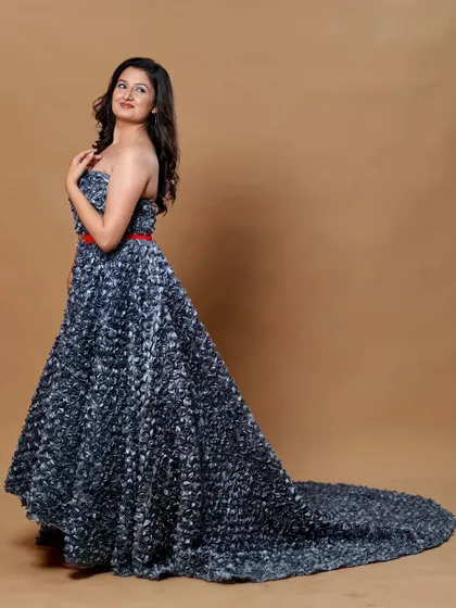 This grey high-low floral gown features a dramatic long tail and a strapless design. The textured floral fabric photographs beautifully against a simple beige backdrop.