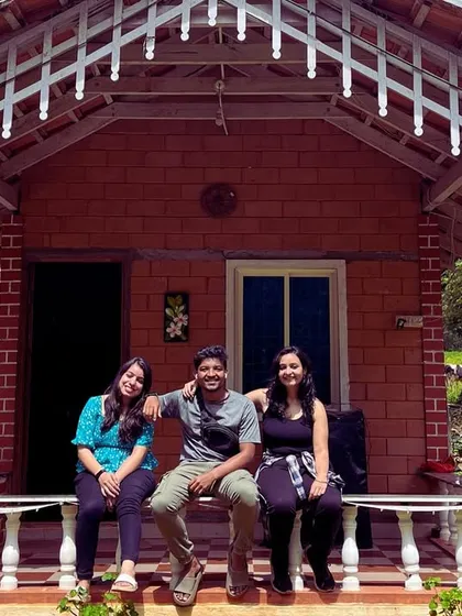 Three travelers relaxing on the porch of a charming brick cottage in Chikmagalur.