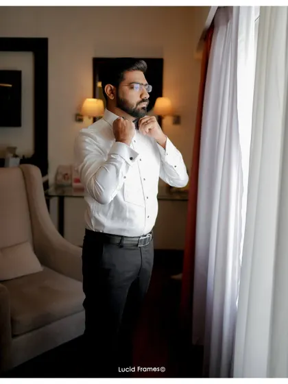 The groom getting ready, adjusting his bow tie in a moment of quiet preparation.
