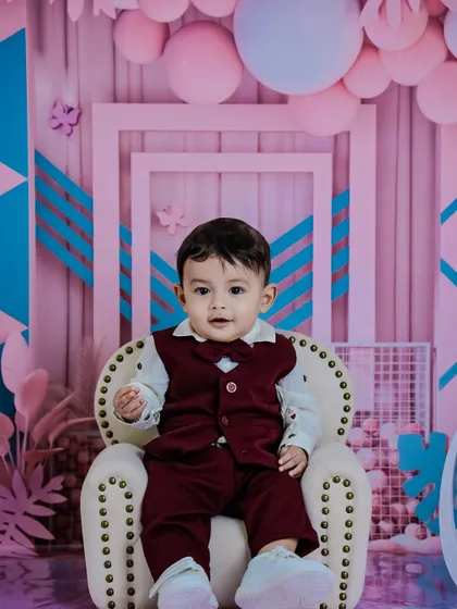 A toddler boy dressed in a sharp vest and bow tie for his milestone photoshoot. The modern pink and blue geometric background adds a stylish and contemporary feel to the portrait.