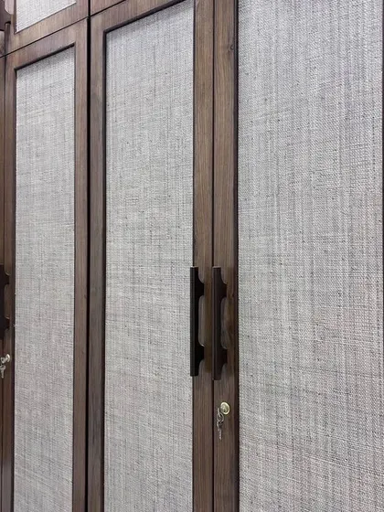 A close-up of a wardrobe with a beautiful fabric-like laminate finish and dark wood trim. This texture adds warmth and a unique tactile quality to the furniture.