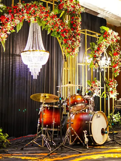 A wider view of the band's stage, showcasing the grand scale of the floral and light design against a dramatic black curtain backdrop.