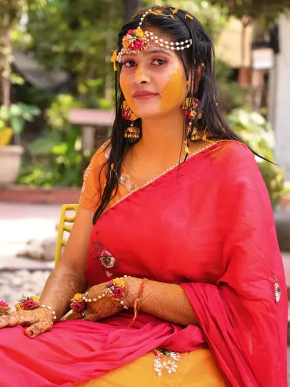 A beautiful portrait of the bride adorned with floral jewelry and haldi, looking directly at the camera with a gentle expression.