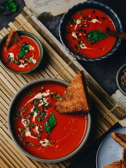 A cozy setup with bowls of warm tomato soup and grilled bread. The dark, moody styling makes the vibrant red of the soup stand out, creating a comforting and hearty feel.