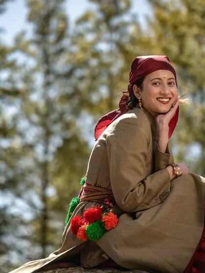 A beautiful solo shot of the woman in her earthy-toned Pahari dress, smiling softly amidst the pine trees.