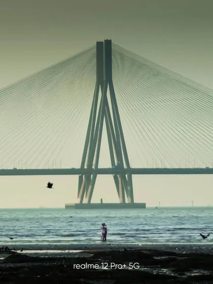 A beautifully framed shot of the Bandra-Worli Sea Link, captured on a mobile phone. The composition with the person in the foreground adds a sense of scale and human element to the grand structure.