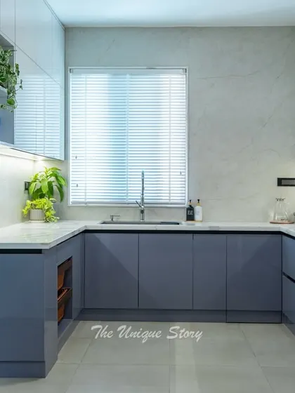 The U-shaped layout of this kitchen maximizes counter space and efficiency. A large window with blinds allows for natural light, while indoor plants on the glossy white cabinets add a touch of freshness.