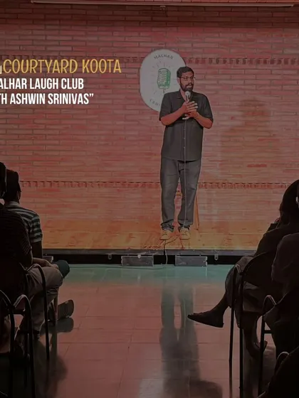 A shot of Ashwin Srinivas on stage during his show for Malhar Laugh Club, with our signature brick wall and MLC logo in the background.