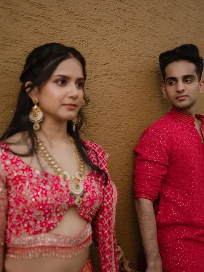 A modern, minimalist portrait of a couple against a simple brown wall, highlighting their contrasting red outfits.