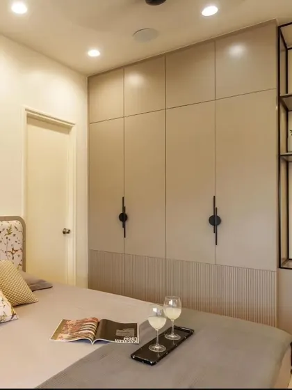 A sleek beige wardrobe with fluted panel details and minimalist black handles. An attached metal open-shelving unit provides a modern contrast and a space for display.