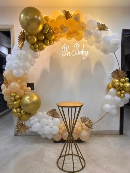 A chic and modern "Oh Baby" circular backdrop for a baby shower, decorated with a white and gold balloon arch.