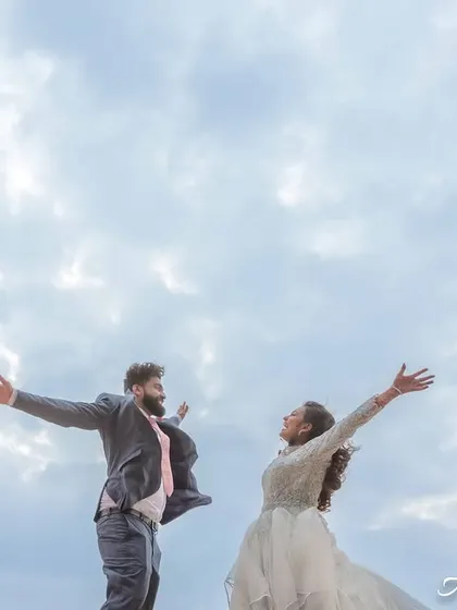 A slightly different angle of the "flying" pose, capturing the dynamic energy and happiness of the couple against the open sky.