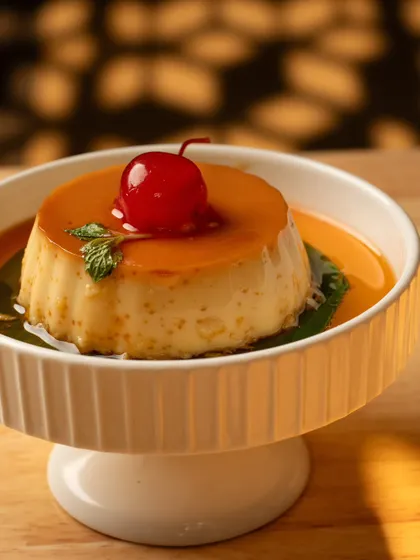 A wobbly, glossy caramel custard with a cherry on top. The beautiful play of light and shadow in this shot gives the classic dessert a dramatic and elegant look.