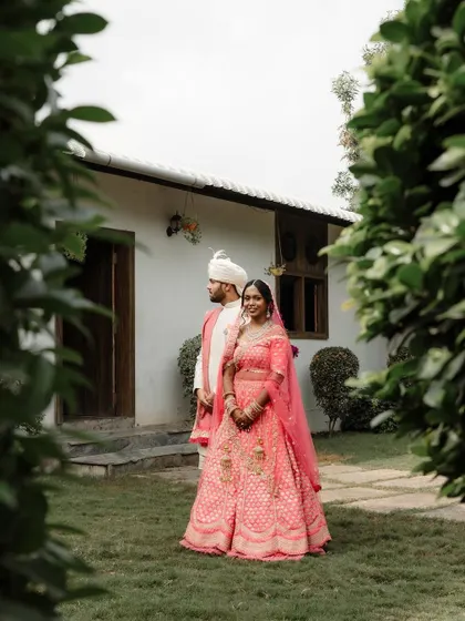 A classic portrait of a couple in their wedding attire, framed by lush green foliage.