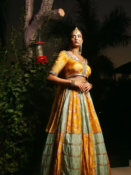 An outdoor, nighttime shot of a model in a traditional lehenga. The lighting highlights the model against the dark, natural background, creating a regal portrait.