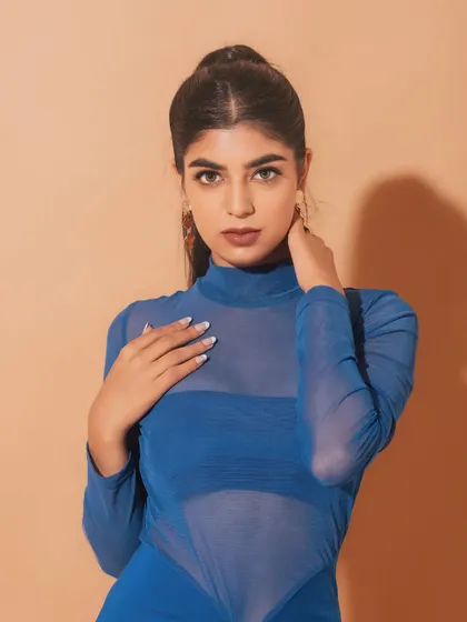 A powerful and confident pose. The makeup is kept clean and minimal, with a focus on a strong brow and a defined lip, complementing the bold blue dress. slight blush and a berry-toned lip.