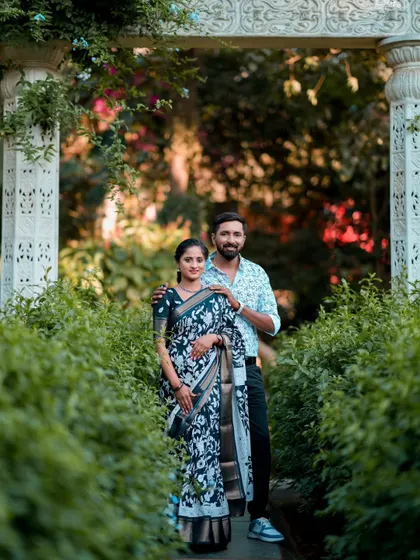 A happy couple posing in a garden archway. Their traditional outfits and the natural surroundings create a fresh and timeless pre-wedding photo.