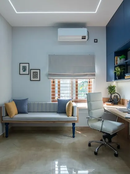This wide shot of the study room highlights the L-shaped desk, the ergonomic white chair, and the comfortable grey bench. The deep blue cabinetry provides a bold contrast to the neutral walls.