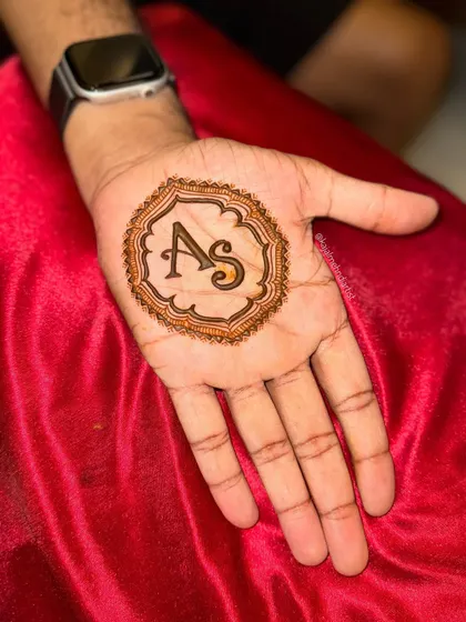 A perfectly executed groom's henna with the couple's initials. The shading technique gives the letters a bold, three-dimensional effect.