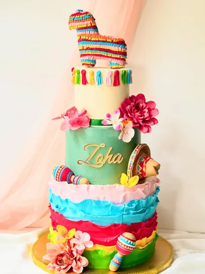 A vibrant four-tiered cake for a Mexican fiesta. The design includes colourful ruffles, a piñata topper, maracas, and a sombrero for a truly festive look.