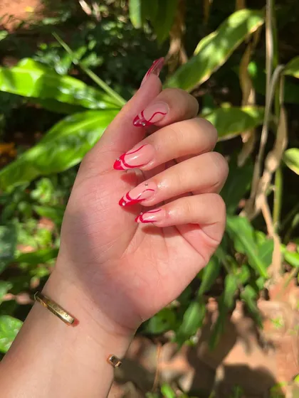 Pinterest-worthy nails. This design features a sheer nude base with abstract red swirls and a delicate French tip.