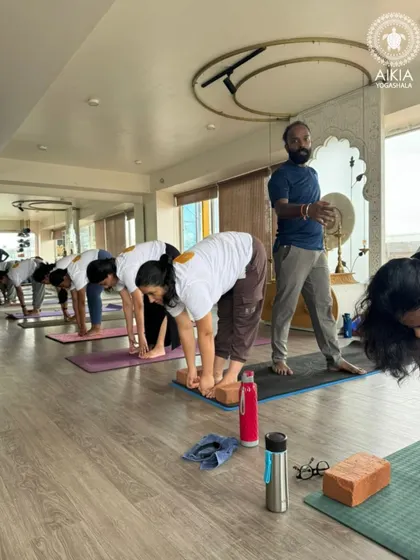 Our guru leads a class of TTC students in a forward-bending sequence, emphasizing synchronized movement and breath. The use of props like blocks is encouraged for proper alignment.