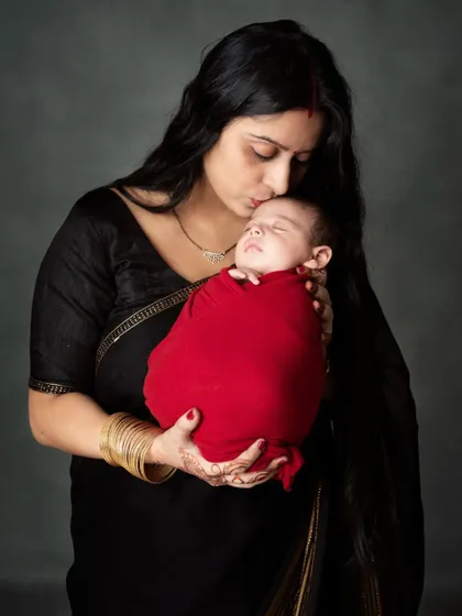 A mother's gentle kiss for her sleeping newborn. A timeless and emotional portrait in a classic black saree.