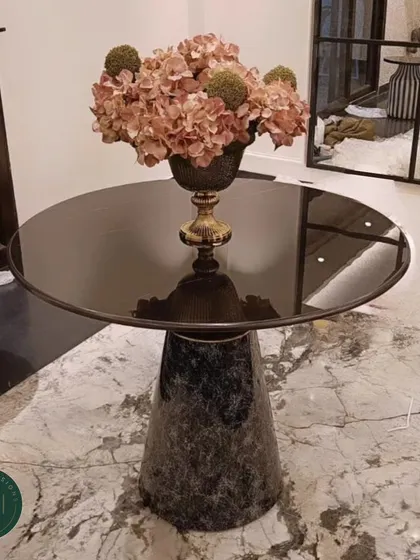 A full shot of our elegant accent table with a marble pedestal base and smoked glass top, styled with a floral arrangement. This shows how our pieces can anchor a decorative vignette.