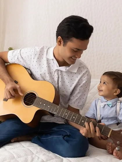 A special bond between brothers. An older brother plays the guitar for his fascinated baby brother during a lifestyle session.