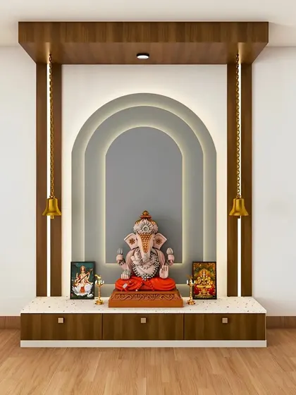 This wall-mounted pooja unit features a unique layered arch backdrop with soft backlighting, creating depth and a sense of divinity. The design is completed with two traditional hanging bells on either side of a Ganesha idol, blending modern forms with classic elements.
