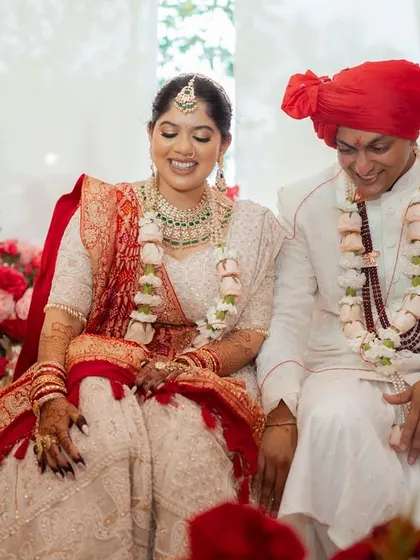 The couple shares a sweet, smiling moment during their wedding ceremony, surrounded by a sea of flowers. Their relaxed joy is a testament to a celebration filled with love and happiness.